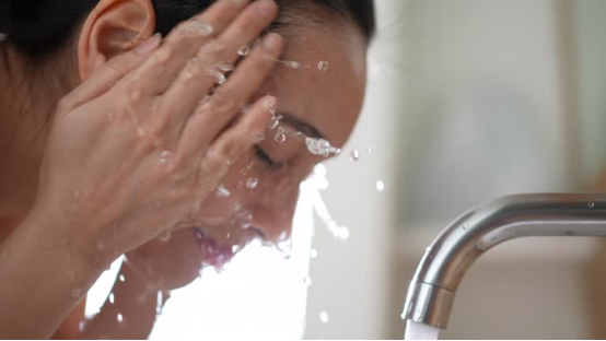 Close-up of a woman washing her face at a bathroom sink, representing a moment in a daily grooming routine where a nose hair trimmer fits in.